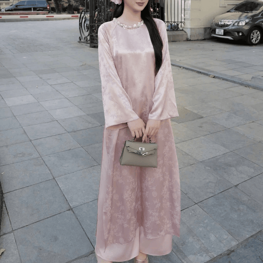 Woman in a light pink dress holding a handbag on a city street.